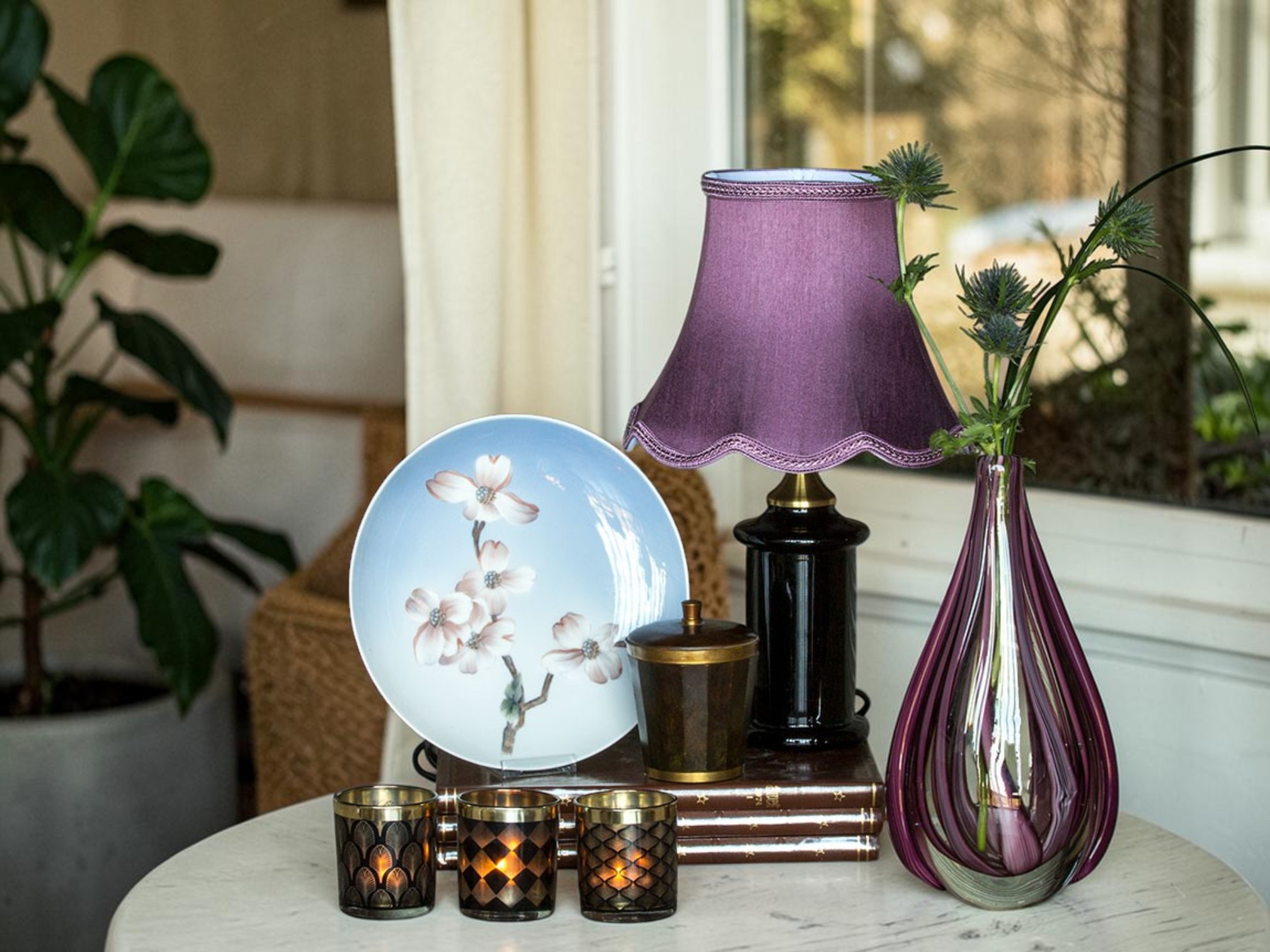 Sort bordlampe med lilla lampeskærm i klassisk skandinavisk design. Lampen står sammen med dekorative interiørdetaljer og kan nemt varieres med forskellige lampeskærme, herunder plisserede og runde modeller, så den passer til mange indretningsstile.
