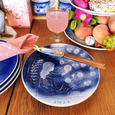 Désirée juleplatte fra 1971 med H. C. Andersen motiv brugt på et forårsbord. Bordet er dækket med lyserød serviet, frugt og kage, der skaber en hyggelig stemning.