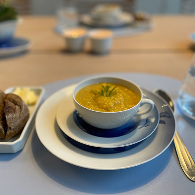 Gammel porcelæns tekop brugt til servering af suppe som forret, anrettet med brød og smør. Kreativ og personlig borddækning.