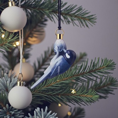 Royal Copenhagen ornament 2021 med blå mejse hænger på juletræet mellem grønne grene, lyse julekugler og varme julelys.