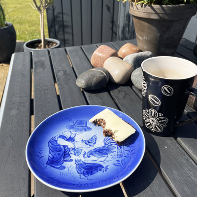 Hverdagsmorgenmad serveret på en blå Désirée Mors Dag platte med motiv. Udendørs opstilling på havebord.