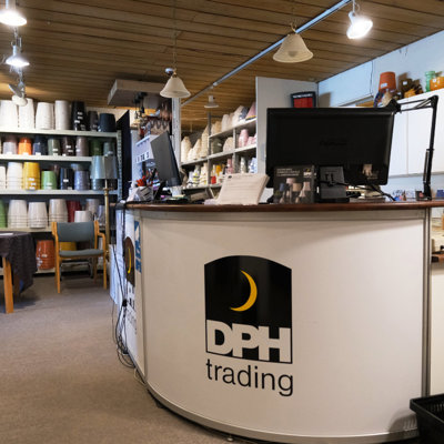 Skranken hos DPH Trading med computer og kundeserviceområde foran store reoler fyldt med lampeskærme i mange farver og størrelser