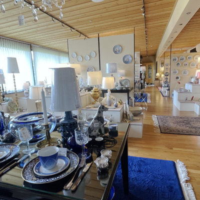 Borddækning med Bing & Grøndahl mindeplatter, Royal Copenhagen Liselund, Holmegaard glas og Hackefors juleklokker – omgivet af lamper, porcelænsfigurer og brugskunst i DPH Tradings butik i Odense N.