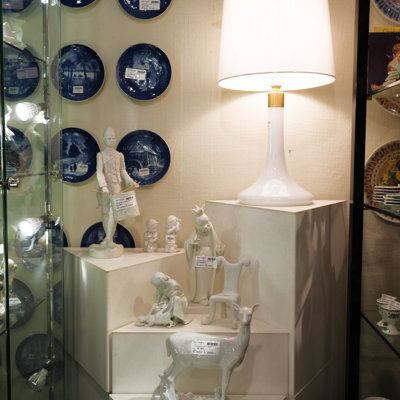 Opstilling med hvide porcelænsfigurer, foran blå juleplatter og under en hvid bordlampe hos DPH Trading i Odense N.