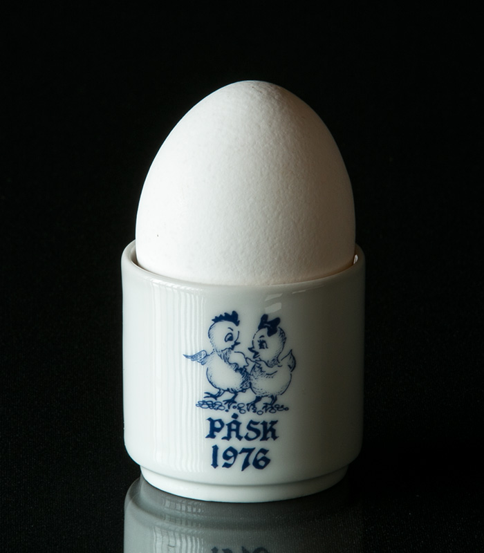 Farverige påskeæggebægere fra Rörstrand, Hutschenreuther og flere, dekoreret med forårsmotiver som kaniner og kyllinger, arrangeret festligt på et påklædt påskebord