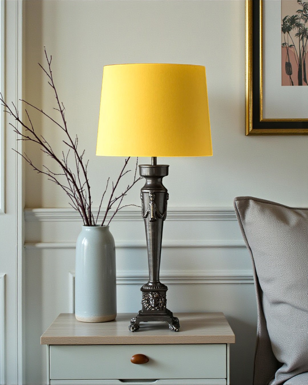 Klassisk bordlampe i patineret bronze med dekorative detaljer og gul lampeskærm placeret ved seng i hyggelig indretning.
