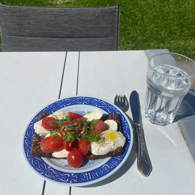 Rörstrand Mors Dag platte brugt som frokosttallerken med rugbrød, mozzarella og tomater. Serveret udendørs i haven med glas vand.