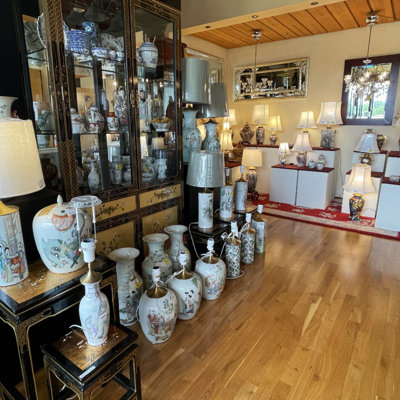 Udstilling med asiatiske lamper og porcelænsvaser i forskellige størrelser hos DPH Trading i Odense N – omgivet af vitrineskabe og opstillinger med klassiske bordlamper.